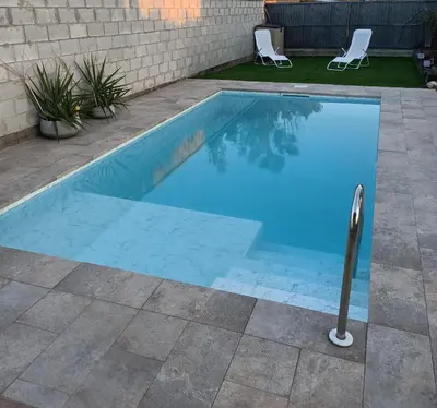 a blue swimming pool in a yard with two chairs at Habitación acogedora y sencilla in El Puerto de Santa María