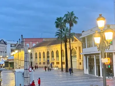 a city street with a yellow building and palm trees at Apartamento Gallo Azul in Jerez de la Frontera