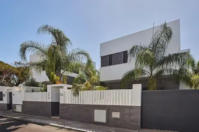 a building with a white fence and palm trees at Villa caracolillo PLAYA Chiclana in Chiclana de la Frontera