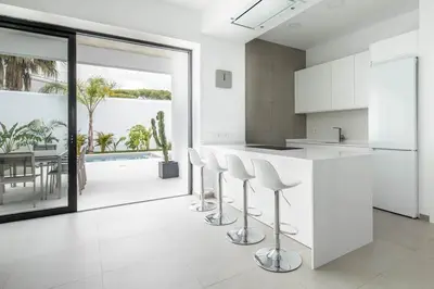 a kitchen with white cabinets and a counter with stools at Villa caracolillo PLAYA Chiclana in Chiclana de la Frontera