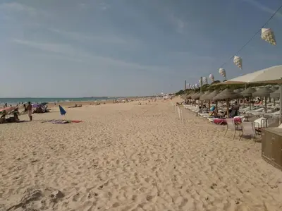 a beach with chairs and umbrellas and people on it at Villa caracolillo PLAYA Chiclana in Chiclana de la Frontera
