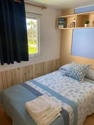 a bedroom with a bed with a blue blanket and a window at Bungalow Mobilhome Agua en Chiclana de la Frontera, Cádiz in Chiclana de la Frontera