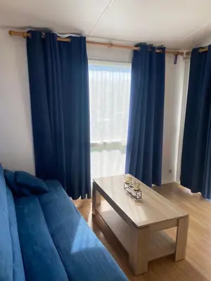 a living room with blue curtains and a table at Bungalow Mobilhome Agua en Chiclana de la Frontera, Cádiz in Chiclana de la Frontera