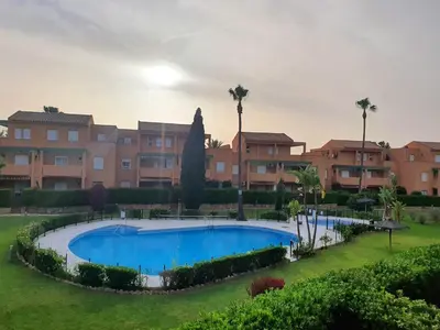 a pool in front of a building with palm trees at Bonito y confortable apartamento Novo Sancti Petri Barrosa Chiclana Cadiz in Chiclana de la Frontera