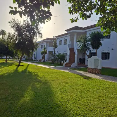 a large white house with a green lawn at Apartamento pinar del atlántico in Chiclana de la Frontera
