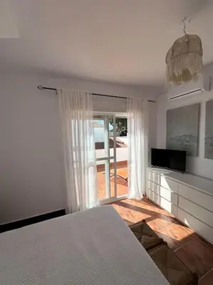 a white bedroom with a bed and a television at Adosado La Loma en Novo Sancti Petri in Chiclana de la Frontera