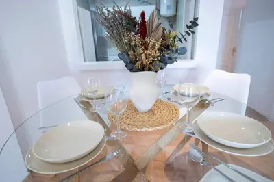 a glass table with white plates and a vase with flowers at GINVA - Apartamento en pleno centro 2 in El Puerto de Santa María