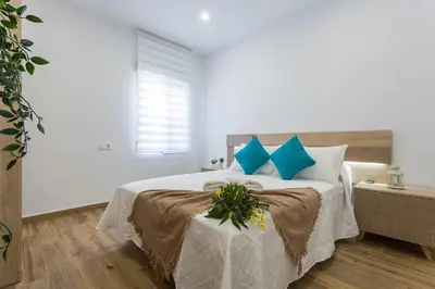 a white bedroom with a large bed with blue pillows at Playa Santa Maria Moderno 3 Rooms in Cádiz
