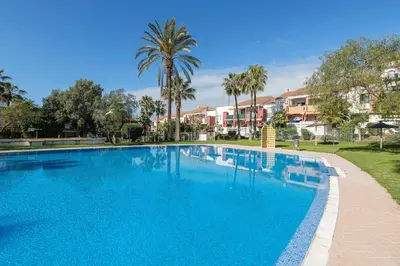 a large blue swimming pool with palm trees and houses at Oasis Playero in Chiclana de la Frontera