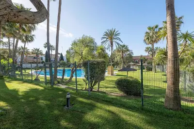 a fence with palm trees and a swimming pool at Oasis Playero in Chiclana de la Frontera
