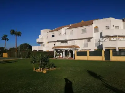 a large white building with a green yard at APARTAMENTO APARTACLUB REFORMADO in Chiclana de la Frontera