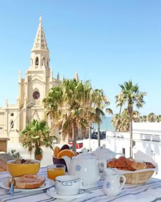 a table with a tea set with a building in the background at Hotel Al Sur De Chipiona by YouRoom in Chipiona