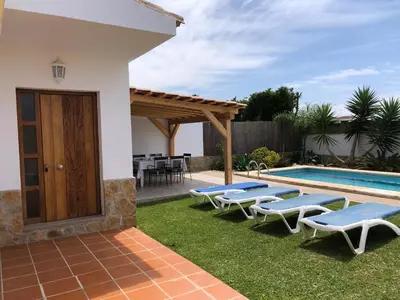 a backyard with a pool with lounge chairs and a house at Villas Dehesa Roche Viejo in Conil de la Frontera