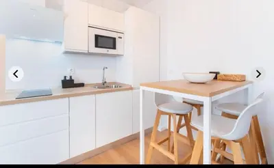 a white kitchen with a table and two stools at ATICO CALLE FARIÑAS in Sanlúcar de Barrameda