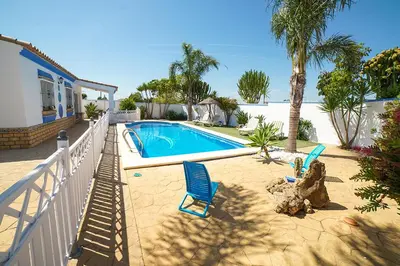 a swimming pool with two blue chairs next to a house at VILLA BANANERA CON PISCINA PRIVADA en CONIL DE LA FRONTERA in Conil de la Frontera