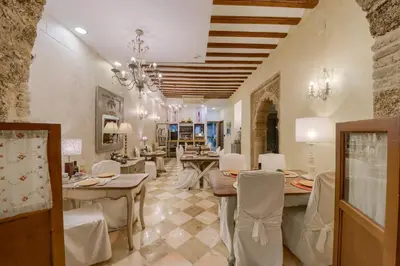 a dining room with white chairs and tables and a chandelier at Hotel Argantonio in Cádiz