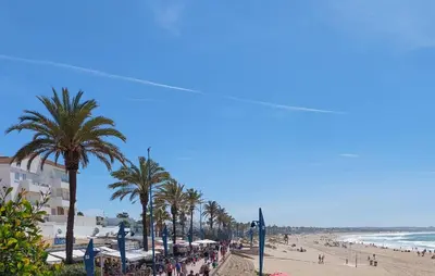 a beach with palm trees and a crowd of people at Nice Home In Chiclana De La Fronter in Novo Sancti Petri