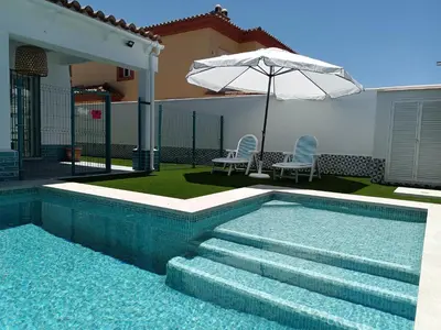 a swimming pool with stairs and an umbrella next to a house at Soto de Vistahermosa in El Puerto de Santa María