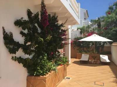 a patio with flowers and an umbrella and a chair at Casa en Sancti Petri junto a playa La Barrosa in Chiclana de la Frontera