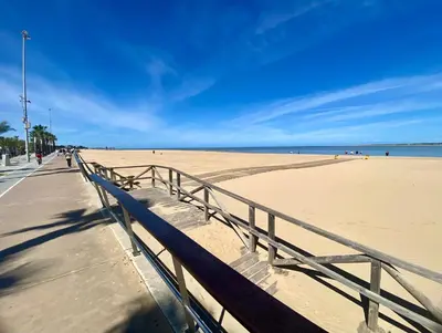 a bench next to a sandy beach with the ocean at ÁTICO Centro y Playa in Sanlúcar de Barrameda