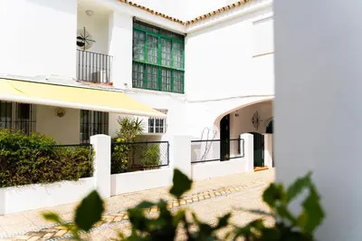 a white building with green windows and a courtyard at Magnífico Dúplex Nueva Andalucía, 3 habitaciones y vistas a la playa in Sanlúcar de Barrameda