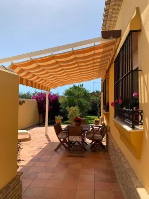 a patio with a table and chairs under a wooden umbrella at La Bilbaina con Piscina, Jardin y Parking Exclusivo 10 in Chiclana de la Frontera