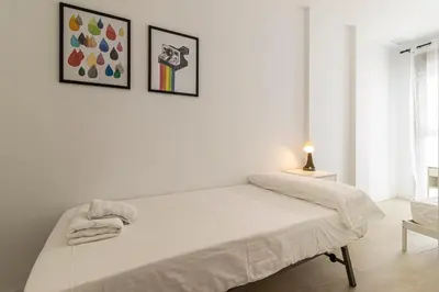 a bed in a white room with two pictures on the wall at Allo Apartments San Clemente Parking Piscina Centro 2 Habitaciones in Jerez de la Frontera