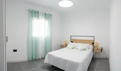 a bedroom with a bed with white sheets and blue curtains at Domus Gades in Chiclana de la Frontera