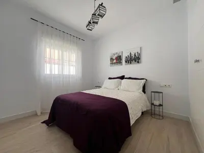 a white bedroom with a bed with a purple blanket at CHICLANA&DISFRUTA in Chiclana de la Frontera