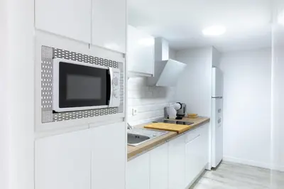 a white kitchen with a microwave and a sink at Falla Suite Bajo in Cádiz