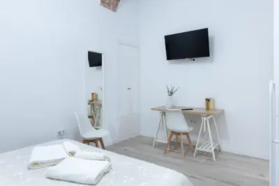 a white room with a bed and a table and a tv at Falla Suite Bajo in Cádiz