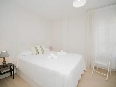 a white bedroom with two beds and a chair at Sibs Sanlucar Maestrante Centrico Ideal Familias in Sanlúcar de Barrameda