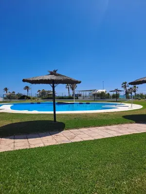 a swimming pool with an umbrella in a park at Apartamento bajo Acuario in Chiclana de la Frontera