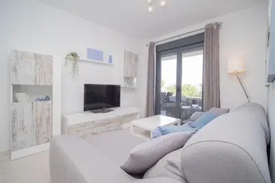 a white living room with a couch and a tv at Calma Beach Bajo de Guía in Sanlúcar de Barrameda