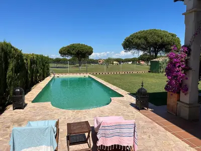 a swimming pool in a yard with two chairs and flowers at Villa Loma Cris y Javi in Cádiz