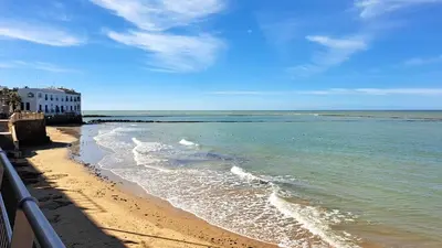 a beach with a building and the ocean at fantástico apartamento chipiona in Chipiona