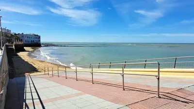 a view of a beach with a fence and the ocean at fantástico apartamento chipiona in Chipiona