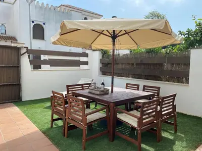 a wooden table and chairs with an umbrella at Casa Playa la Jara in Sanlúcar de Barrameda