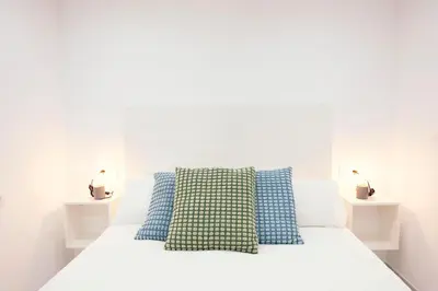 a white bed with two blue pillows on it at Summerlandrota Veracruz28 in Rota