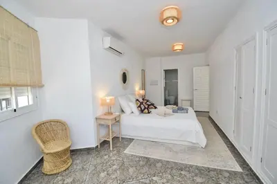 a white bedroom with a bed and a chair at Chici - Holiday Chiclana in Chiclana de la Frontera