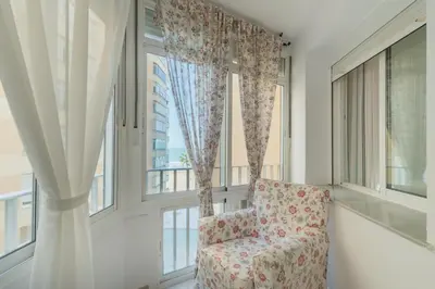 a room with a chair and large windows at Disfruta Vacaciones Familiares Piso Frente al Mar in Cádiz