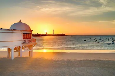 a lighthouse on the beach with people in the water at Disfruta Vacaciones Familiares Piso Frente al Mar in Cádiz