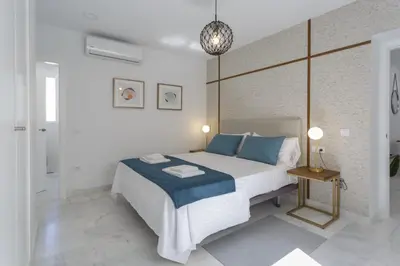 a white bedroom with a large bed with blue pillows at BRUJULA ground floor indoor apartment by Cadiz4Rentals in Cádiz