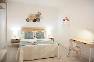 a white bedroom with a bed with a desk and a desk at Sanlúcarsun Apartamento en el centro in Sanlúcar de Barrameda