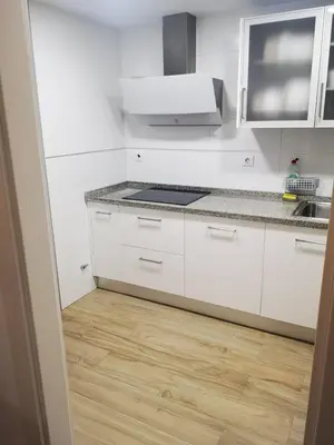 a kitchen with white cabinets and a wooden floor at Aires de Cadiz Apartamento a estrenar in Cádiz