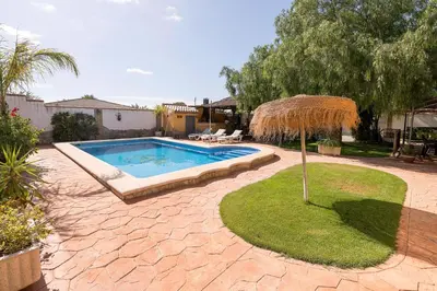a swimming pool with a straw umbrella in a yard at La Redondela in Chiclana de la Frontera