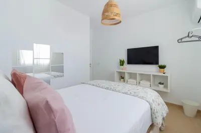 a white bedroom with a bed and a tv at El paraíso de los Suᴇños in Chiclana de la Frontera