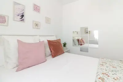 a white bedroom with a white bed with pink pillows at El paraíso de los Suᴇños in Chiclana de la Frontera