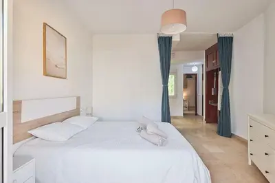 a bedroom with a bed with white sheets and blue curtains at El Palmeral Ha Free Parking in Cádiz