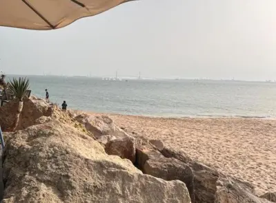 a beach with rocks and the ocean and an umbrella at Chalet Puerto Sherry in El Puerto de Santa María